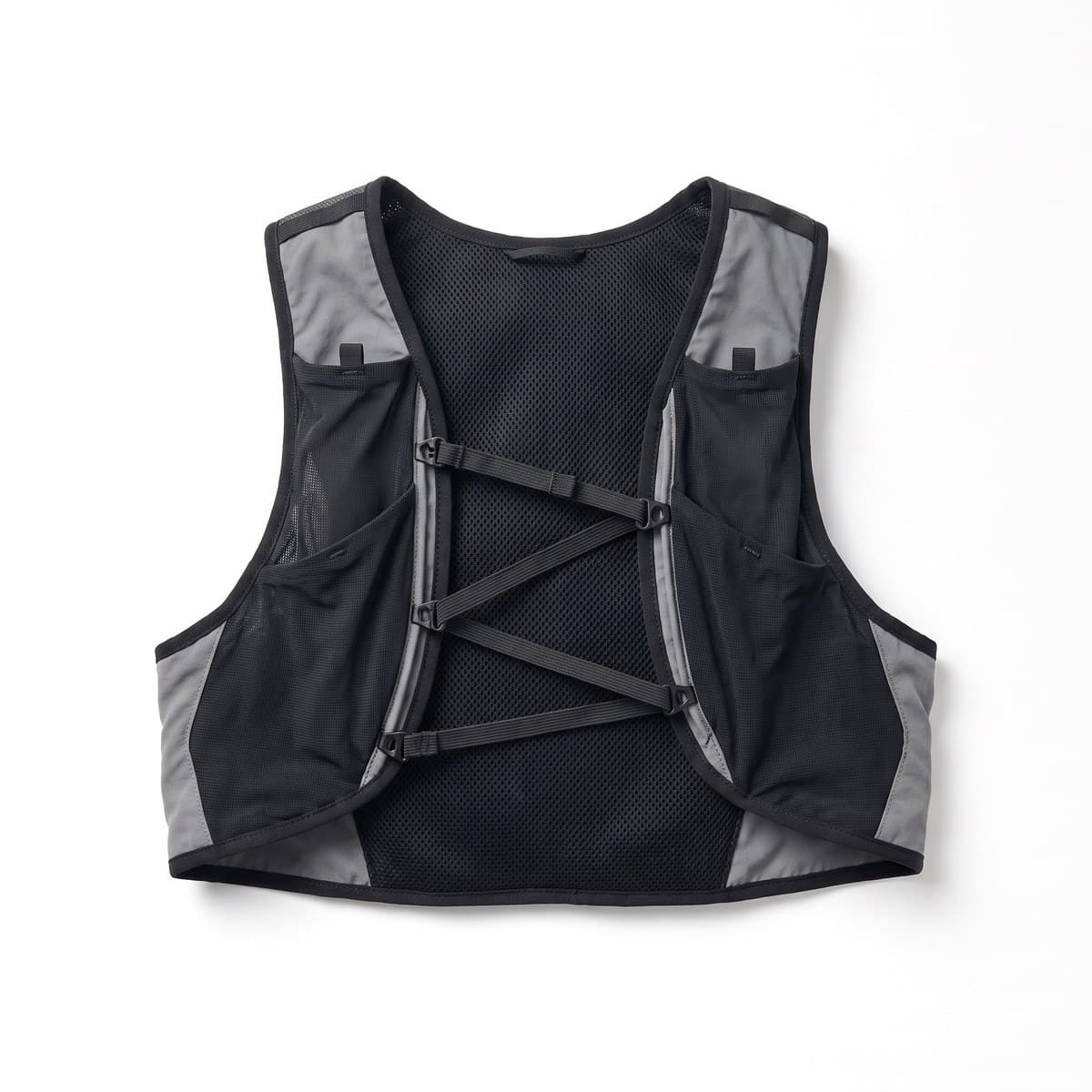 A black trail running vest with grey panels, two front flask pockets and elastic sternum straps, laid flat